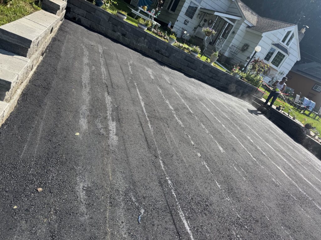Fresh asphalt driveway installation with stone retaining wall and house in Connecticut.